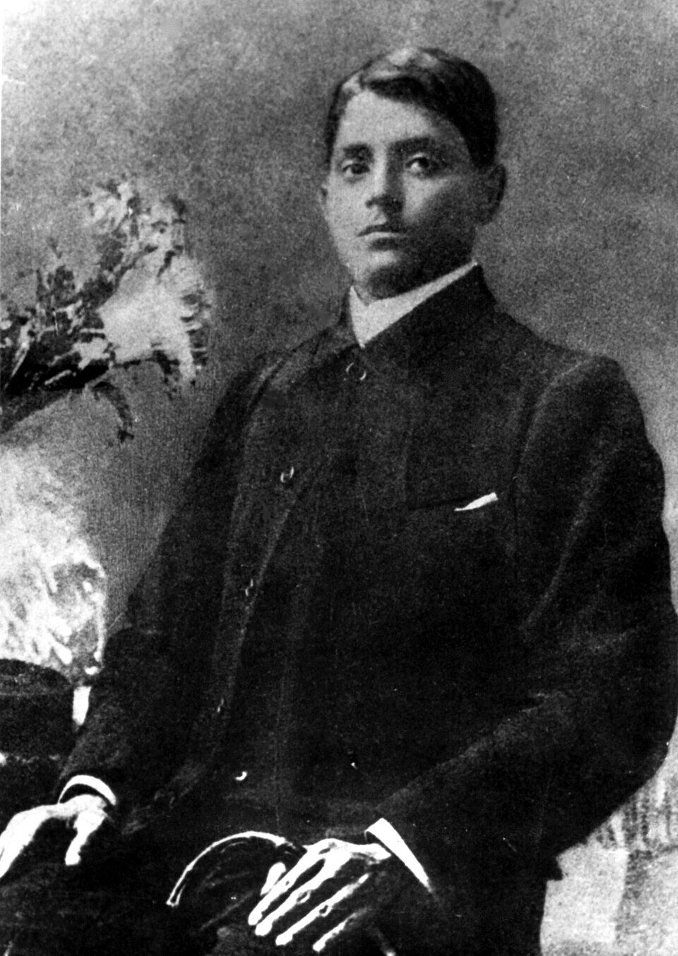 Seated studio portrait of Jatindranath Mukherjee in a dark buttoned coat, hands resting in his lap, photographed in Darjeeling.