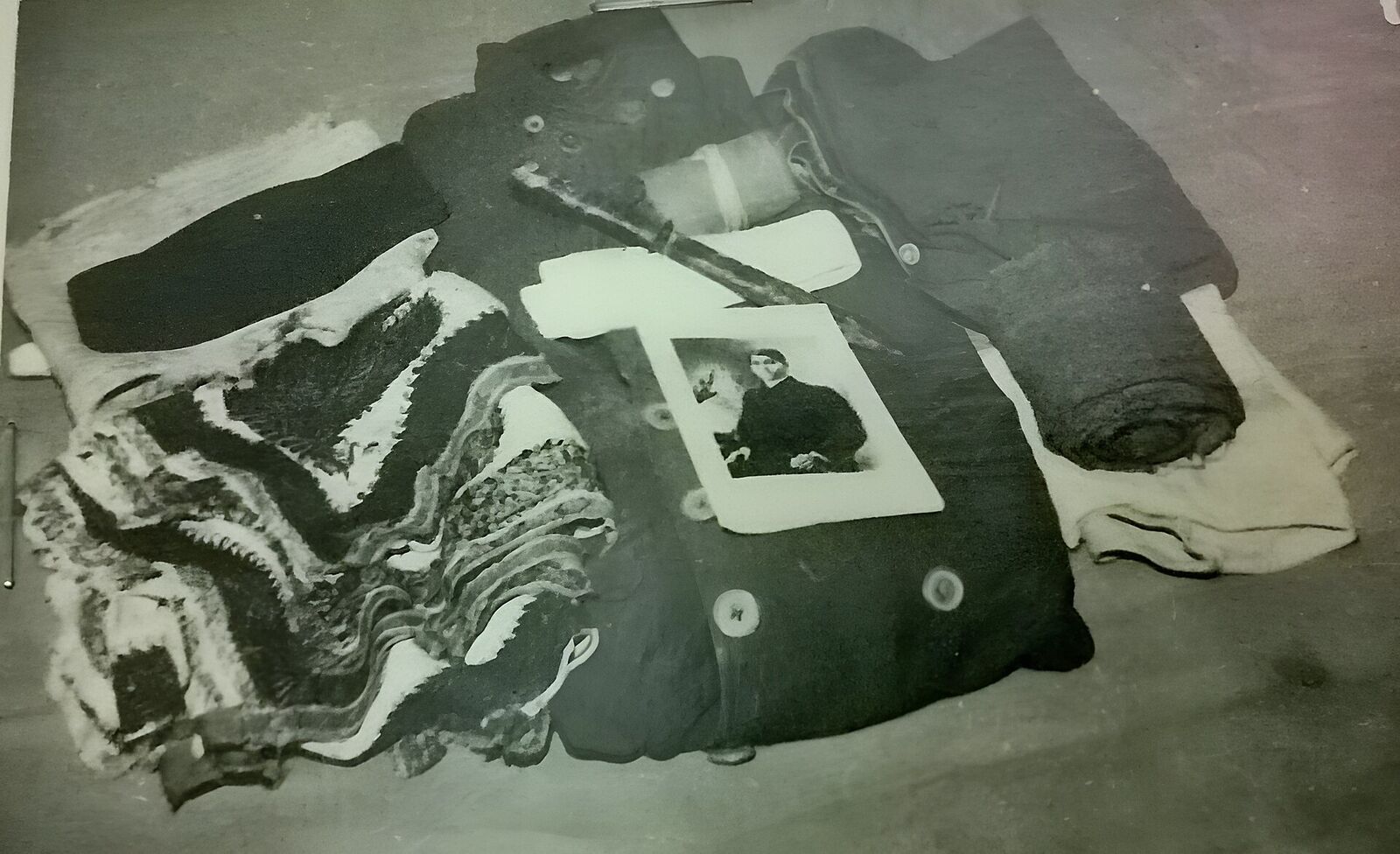 Preserved garments and cloth laid flat in a museum display, photographed from above, with a small portrait resting on top.